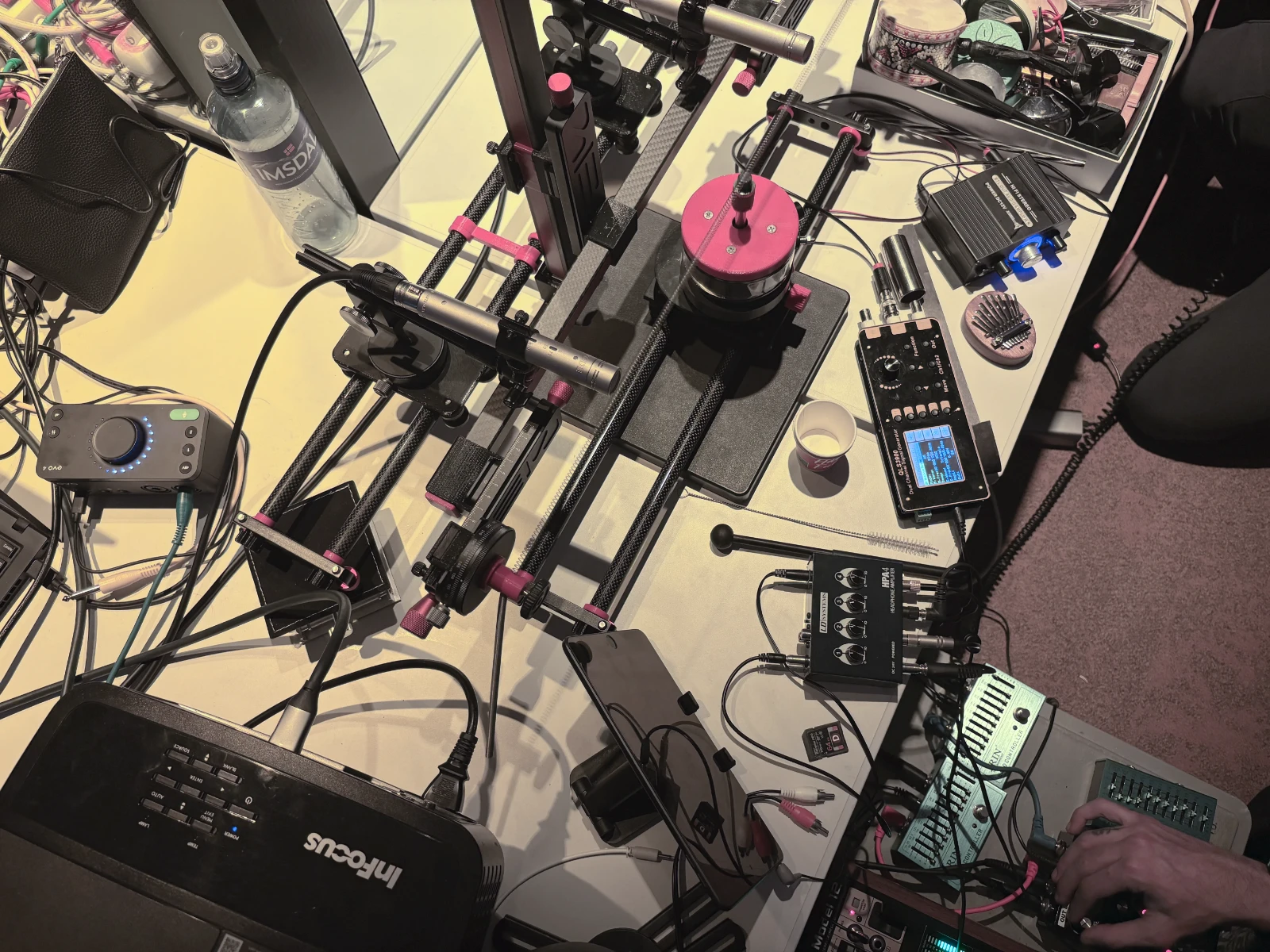 A table full of instruments. Among them a wire being rubbed by a rod with a microphone pointing at it.