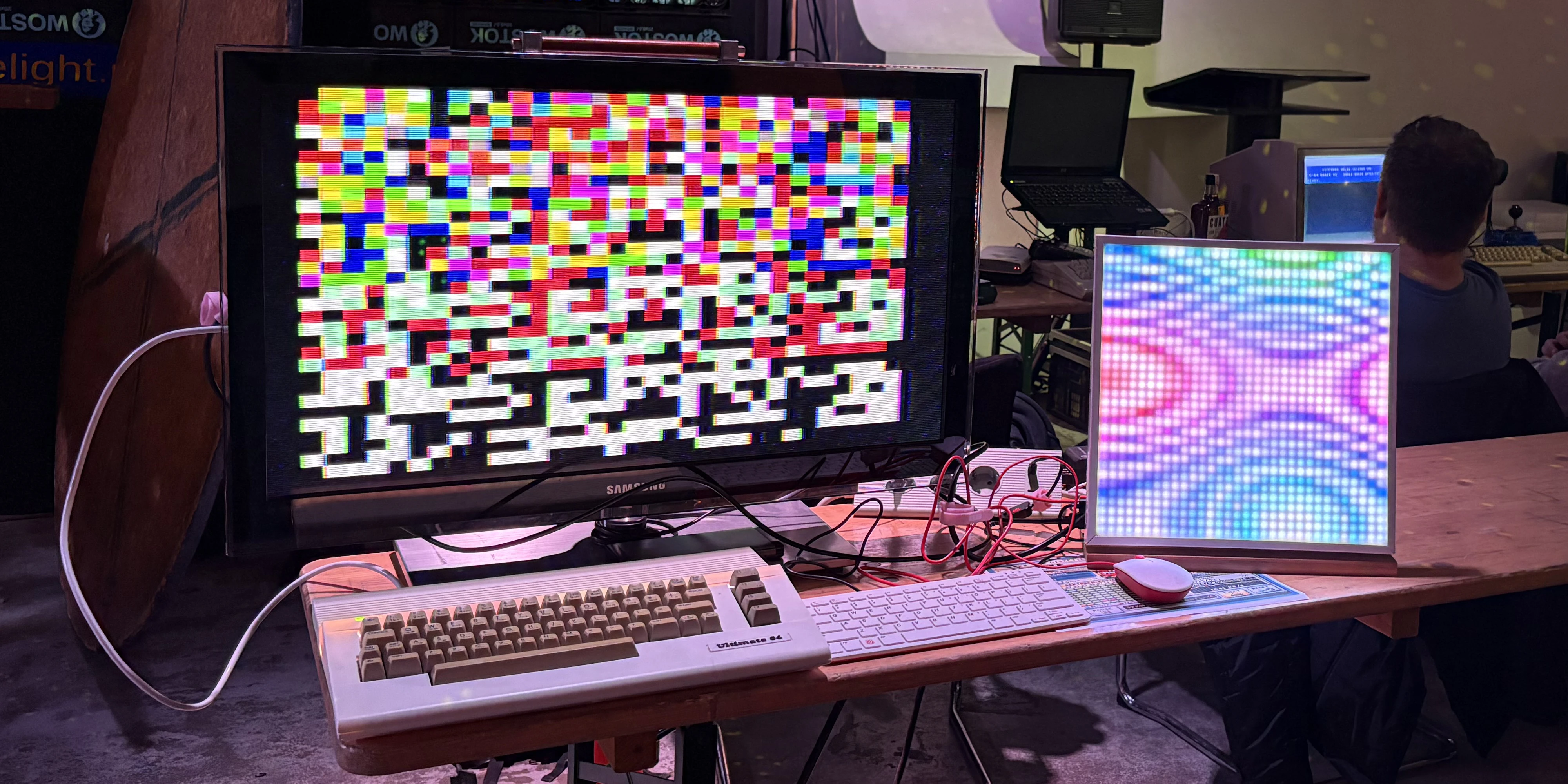 A massive monitor attached to a pimped C64 with a Raspberry Pi 400 and a custom-built computer attached to a pixelated display.