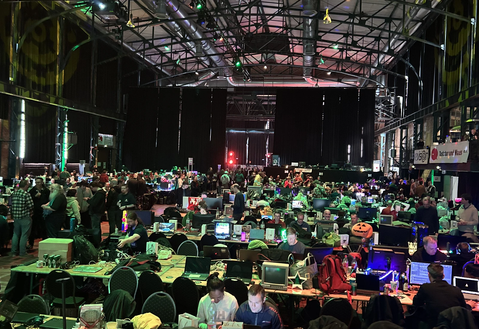 The main hall of the Revision 2025 demoparty, showing table rows filled with people working on laptops.