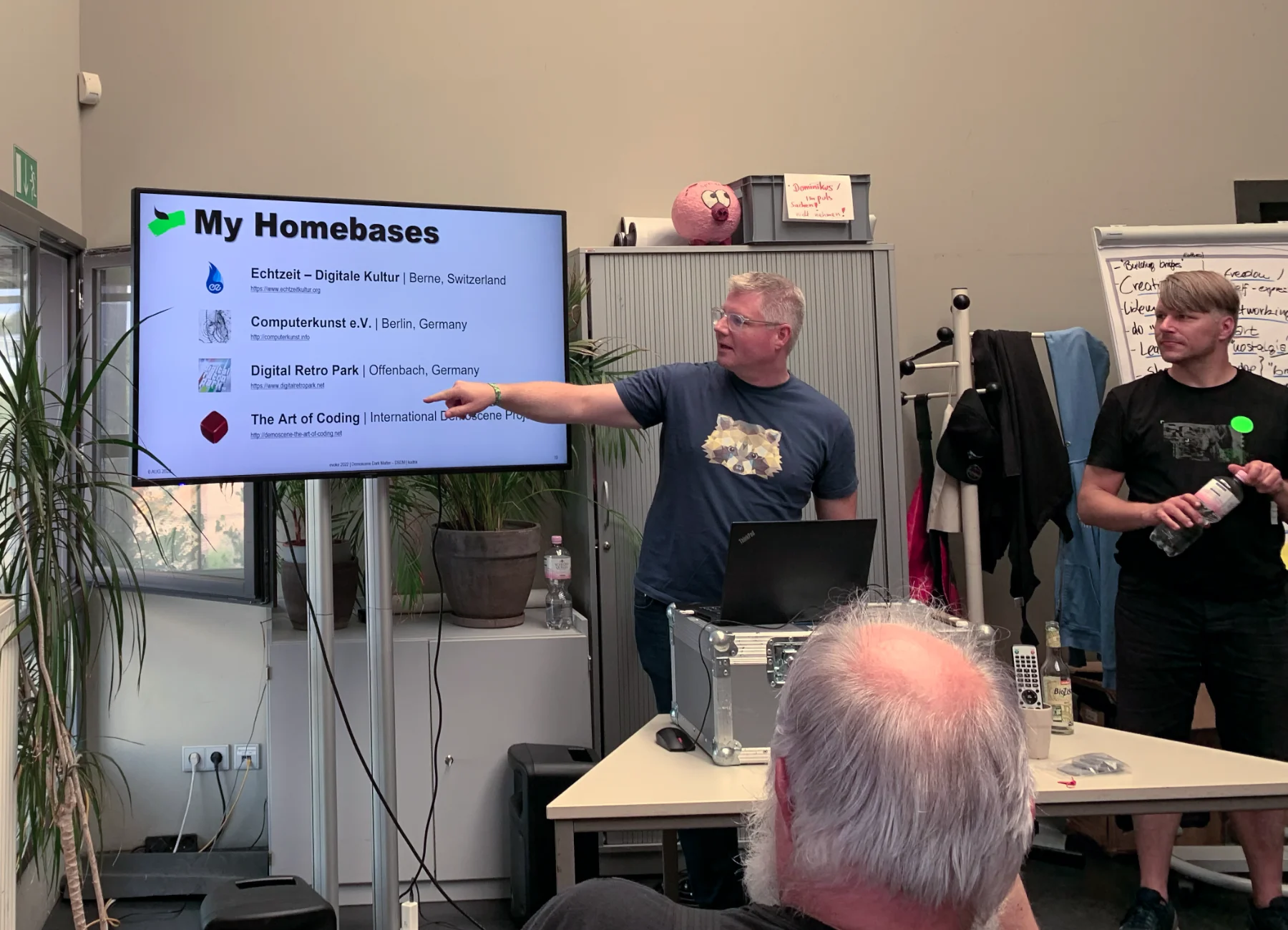 A white haired gentleman wearing glasses in the seminar room pointing at the screen.