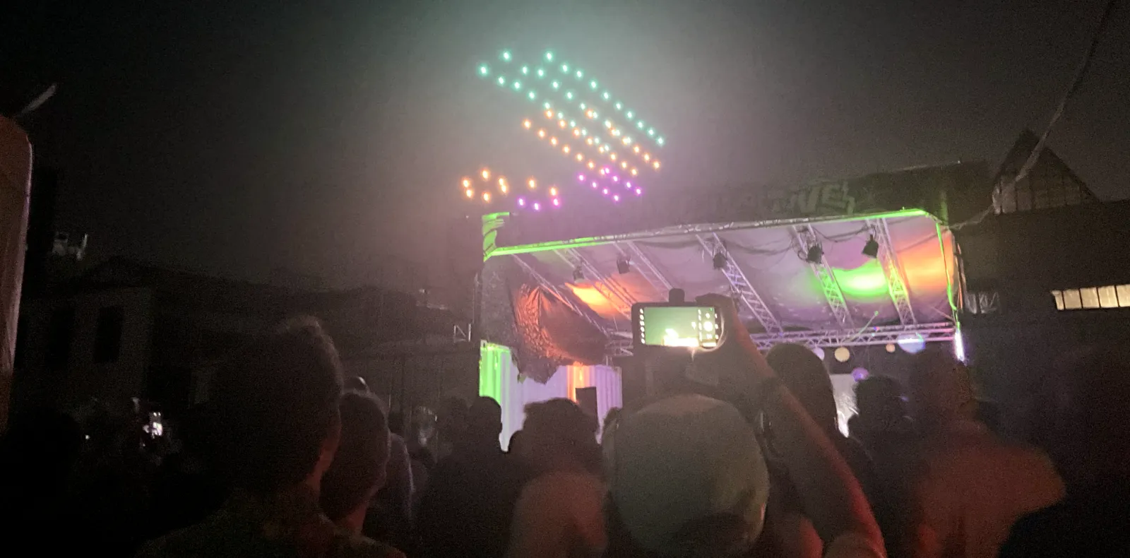 Illuminated drones hovering in the black night sky above the party location.
