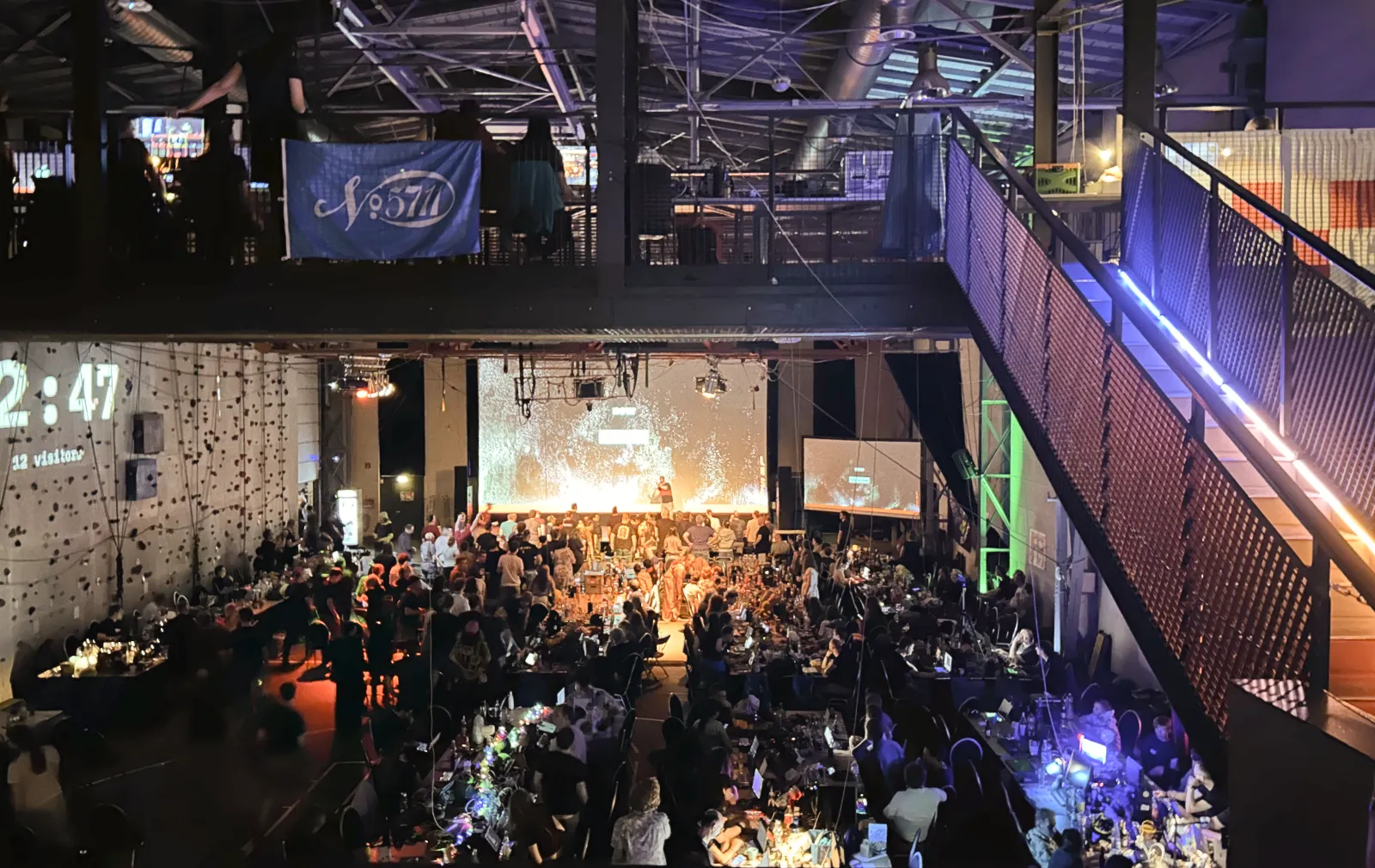 The dark main hall of the AbenteuerHallenKALK full of long tables with piles of computers on them and more than 400 participants.