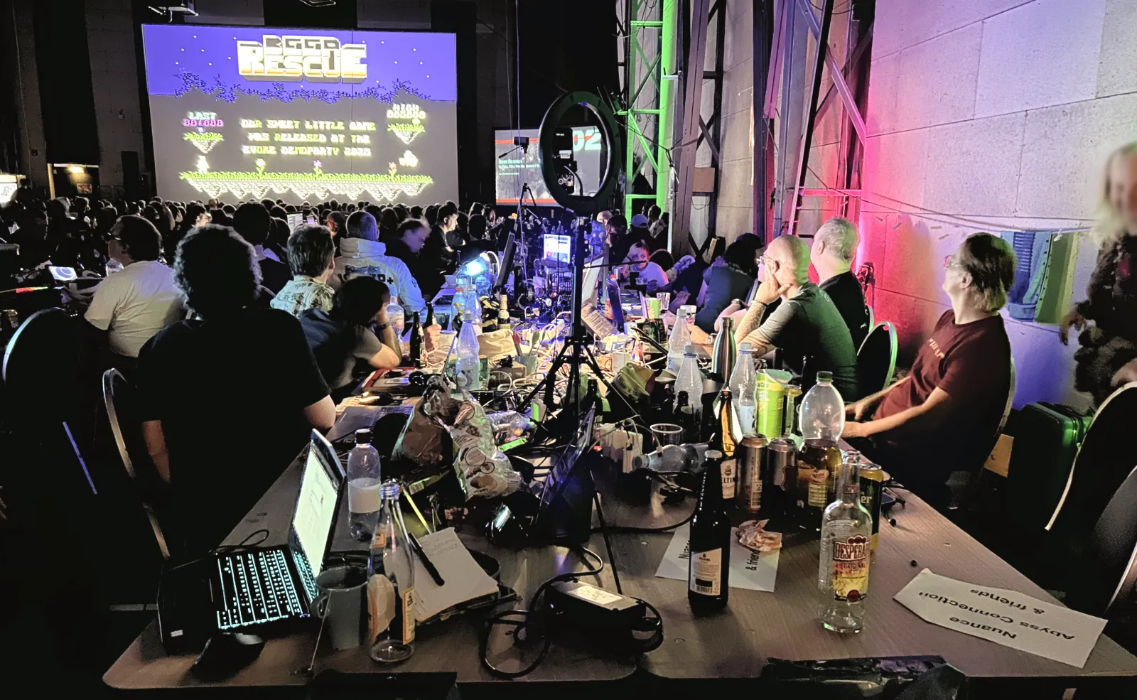 Another perspective of a table with demosceners with their computers and equipment watching the competition entries in the main party hall.