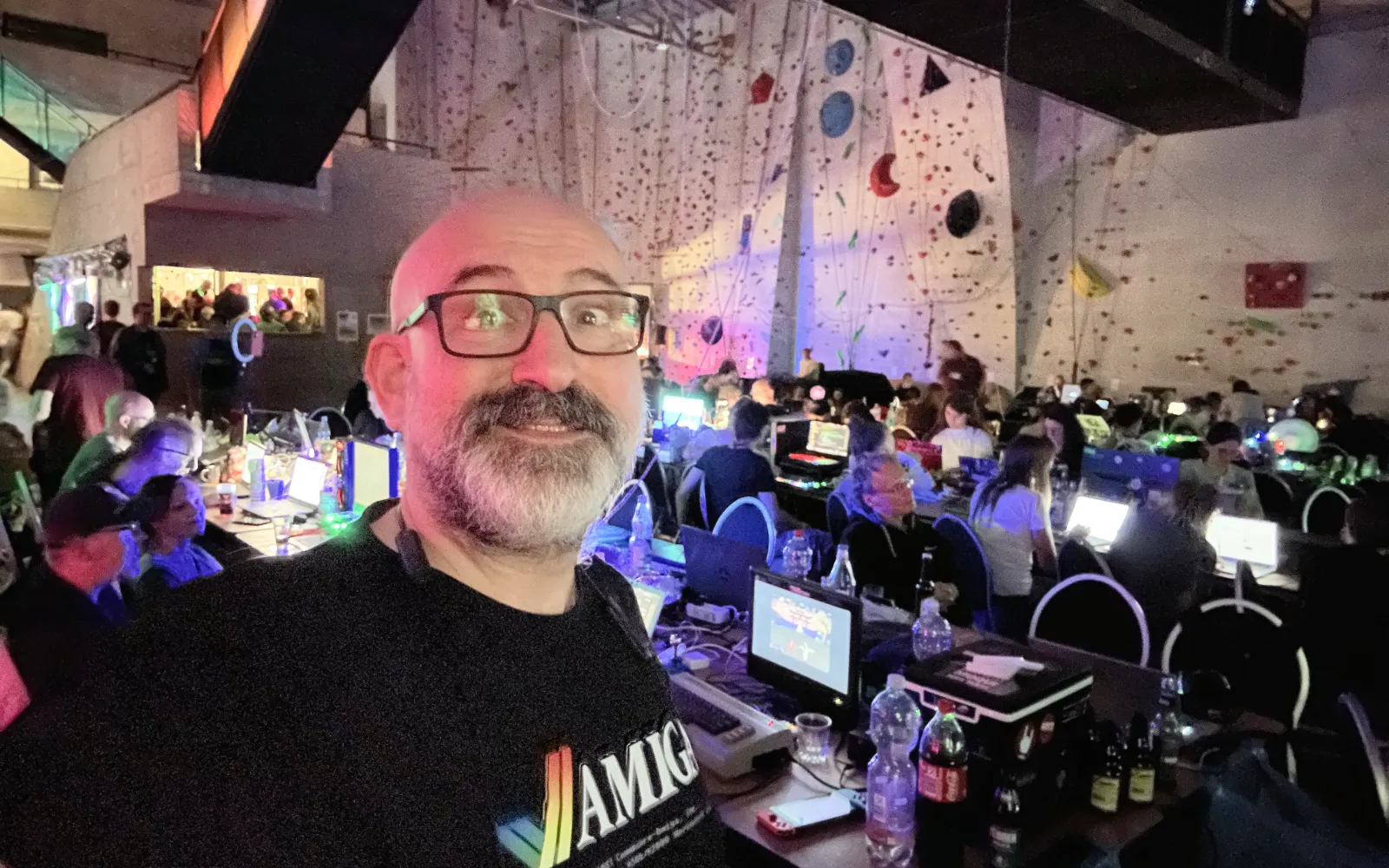 Marin with his beard and bald head facing the camera standing in front of the hustle and bustle of the demoparty