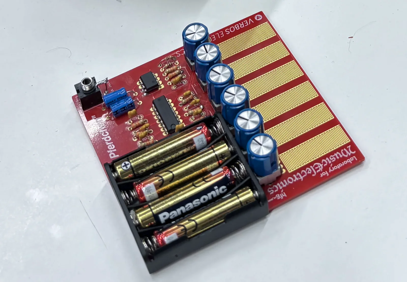 The red Pferdchen PCB synth with golden capacitive touch strips, next to a Benjolin and a printed patch diagram.