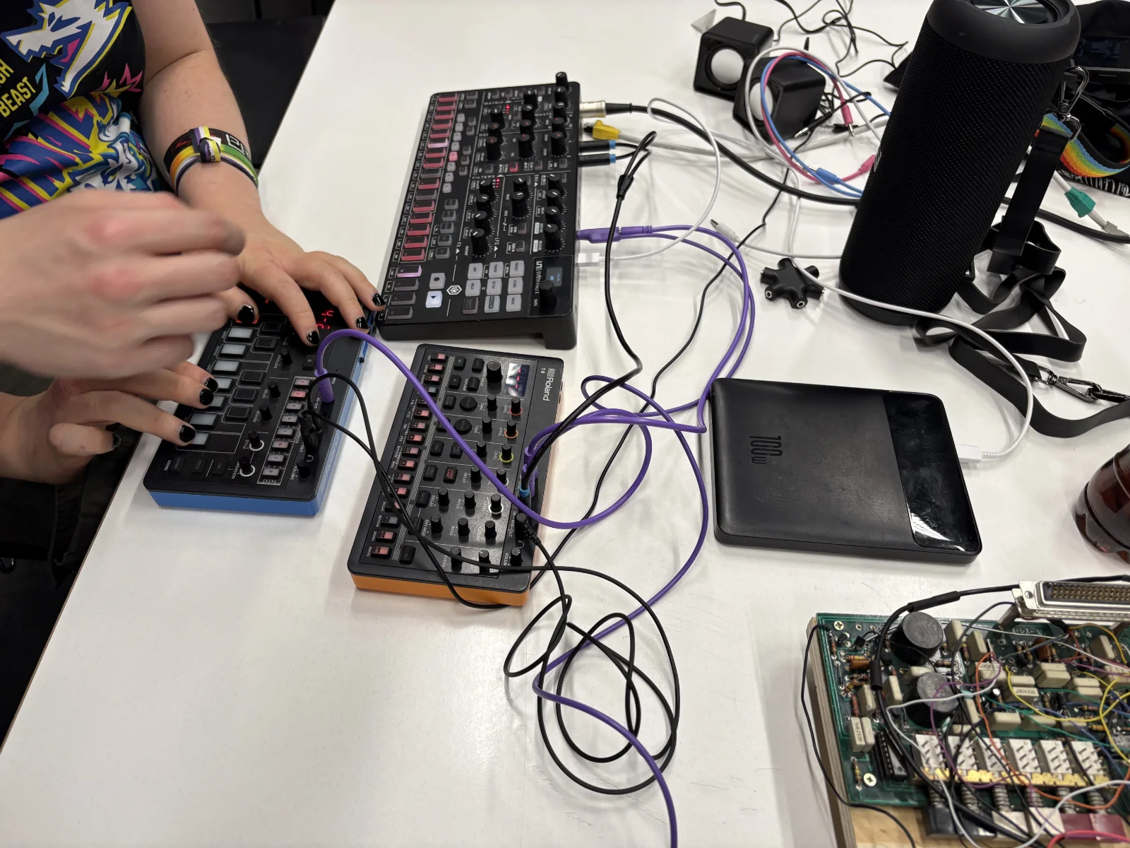 Roland AIRA Compact T-8 Beat Machine and J-6 Chord Synthesizer patched together with purple sync cables on a workshop table.