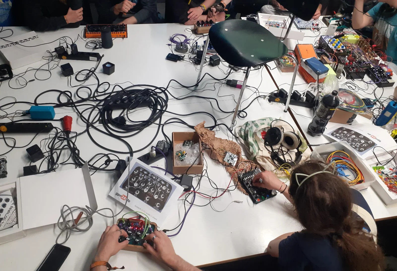 Overhead view of a workshop table with Benjolin synths, power strips, patch cables, and a printed gpn24.de instruction diagram.