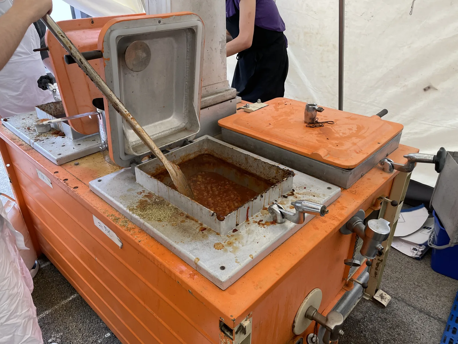 The orange field kitchen unit with a wooden spoon resting in a steel insert of goulash, sponges and washing-up liquid on the surface.