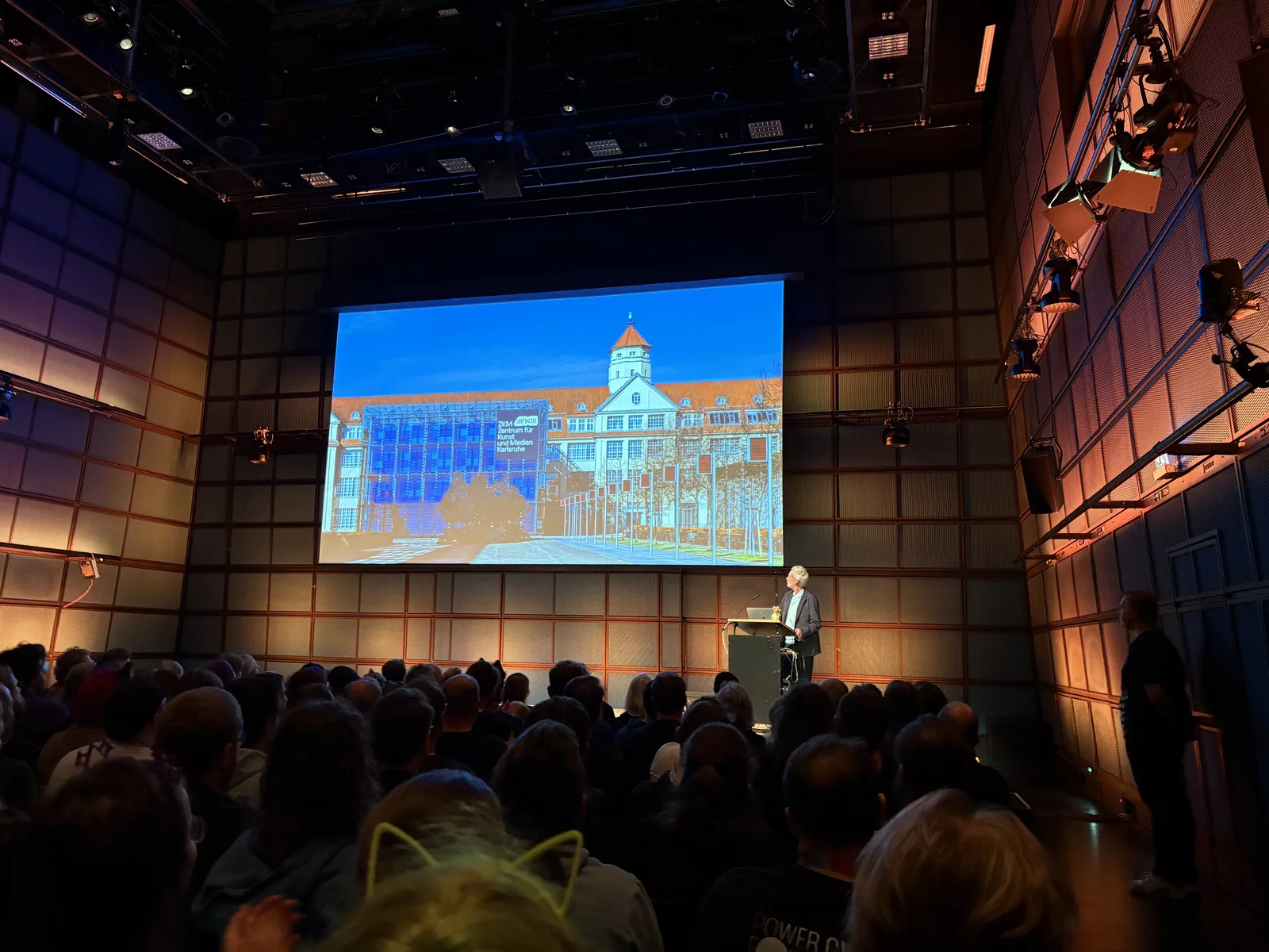 The packed Medientheater auditorium during the GPN24 opening ceremony, a speaker at a podium in front of a large screen.
