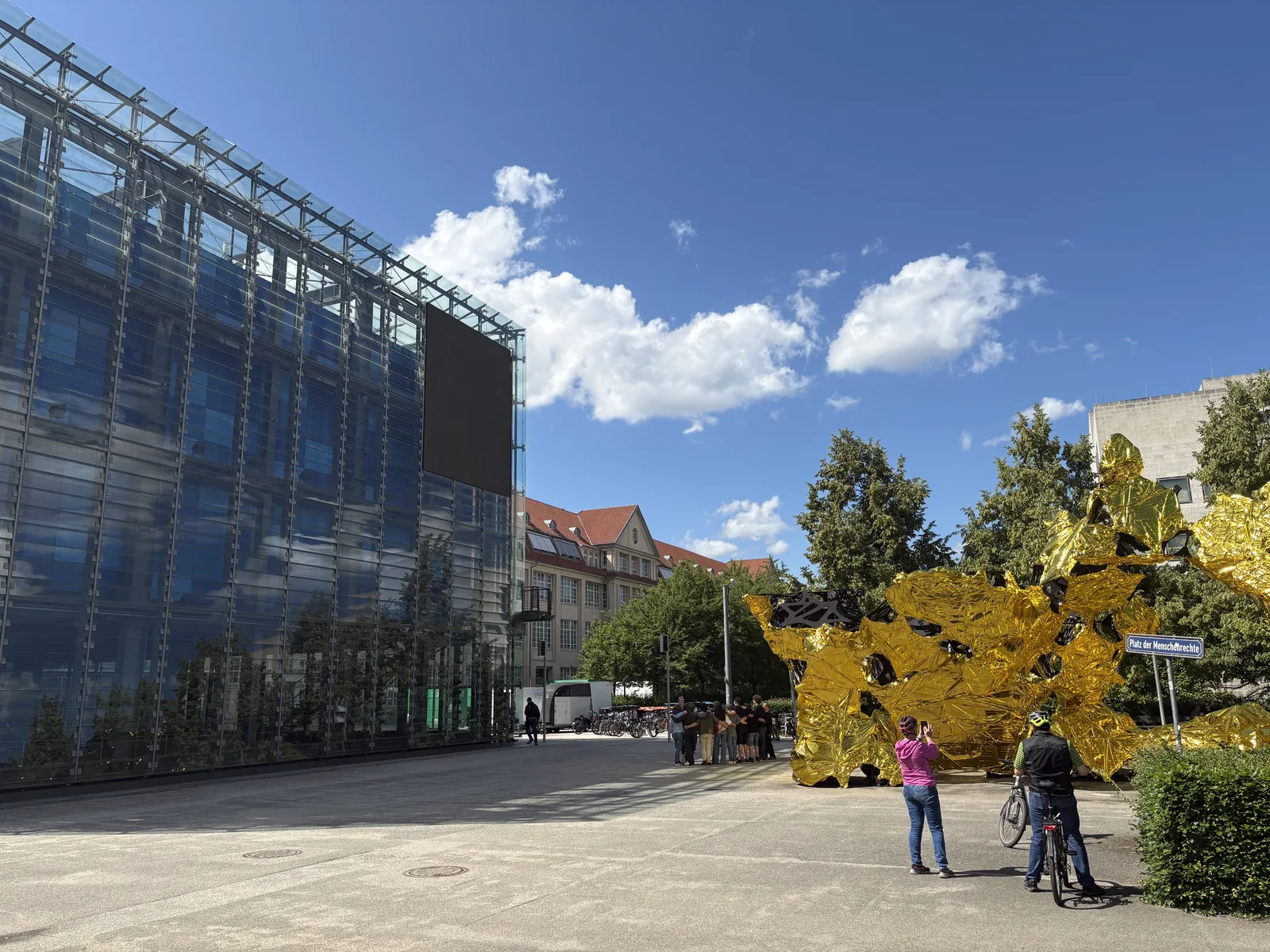 The ZKM building exterior with a golden sculpture and visitors on the plaza under a blue sky.