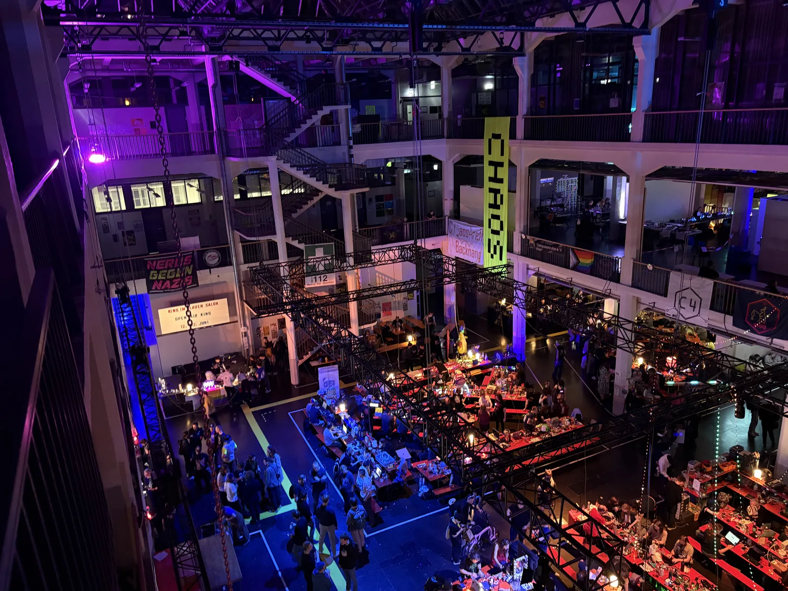 Overhead view of the ZKM main hall at night, a lit-up CHAOS sign hanging over rows of tables.