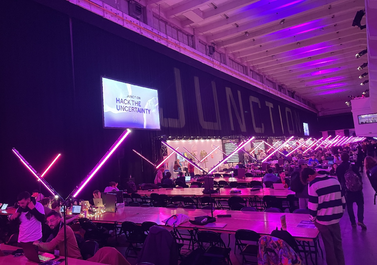 Photo of the Kaapelitehdas event location with rows upon rows of tables and the hackathon participants preparing for the start of the event.