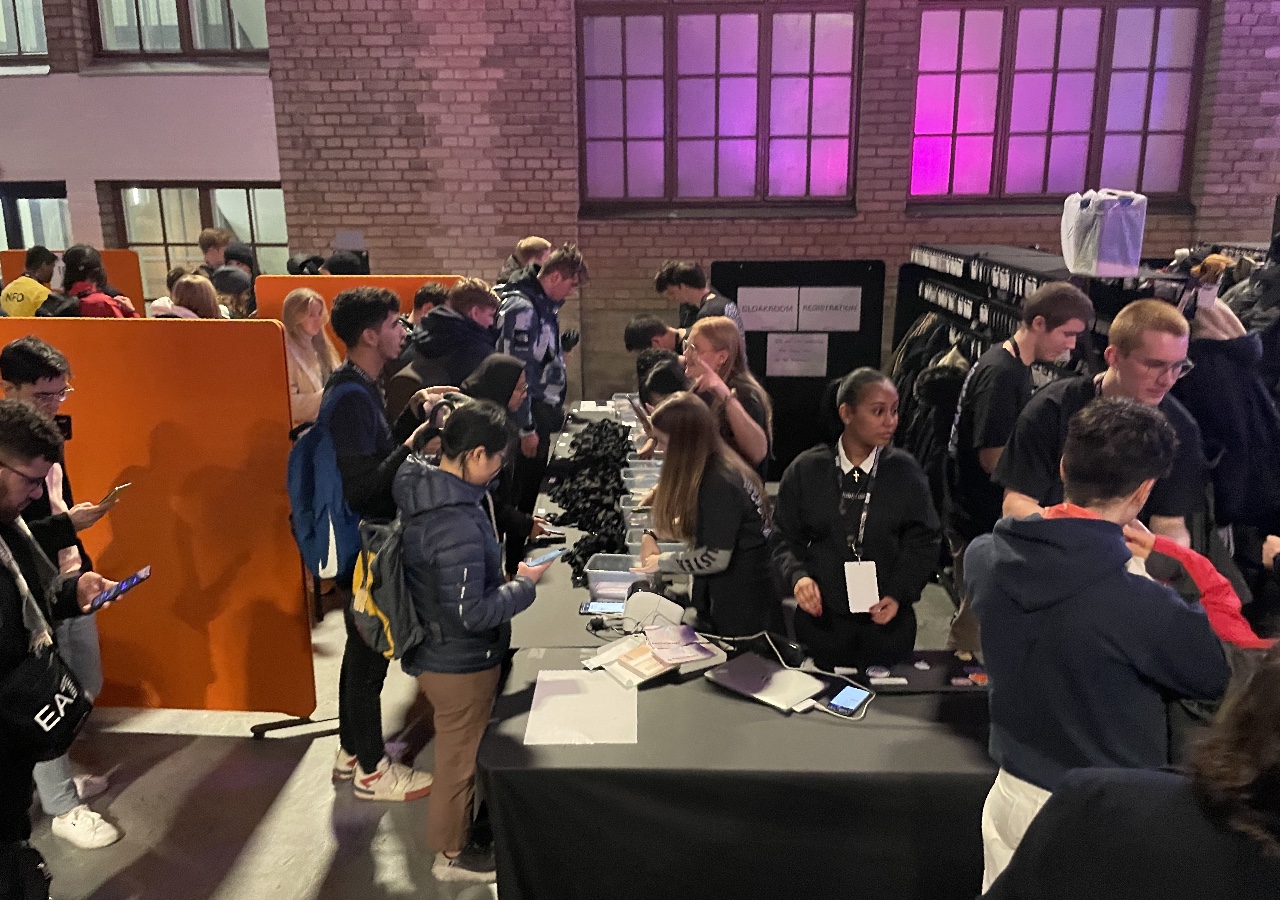 A photo showing a stand in a large indoor event location with young volunteers who are handling the registration at the hackathon.