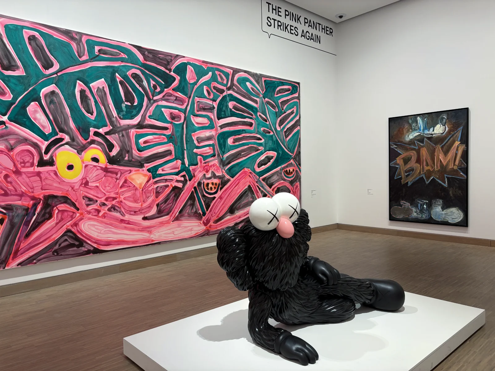 A large painting of the Pink Panther striking a reclining pose next to a KAWS BFF sculpture.