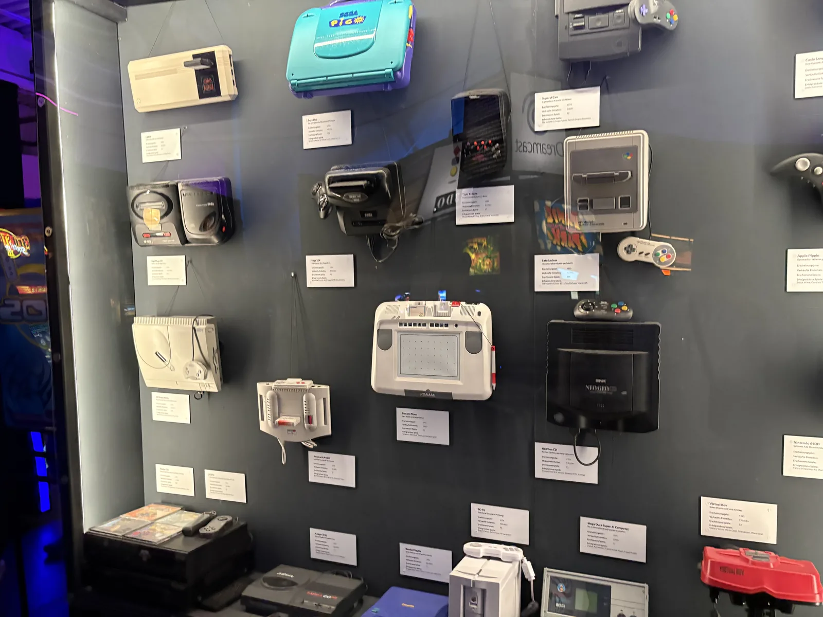 A dark wall display of handheld and home consoles with small info labels, including a red Virtual Boy at the bottom.