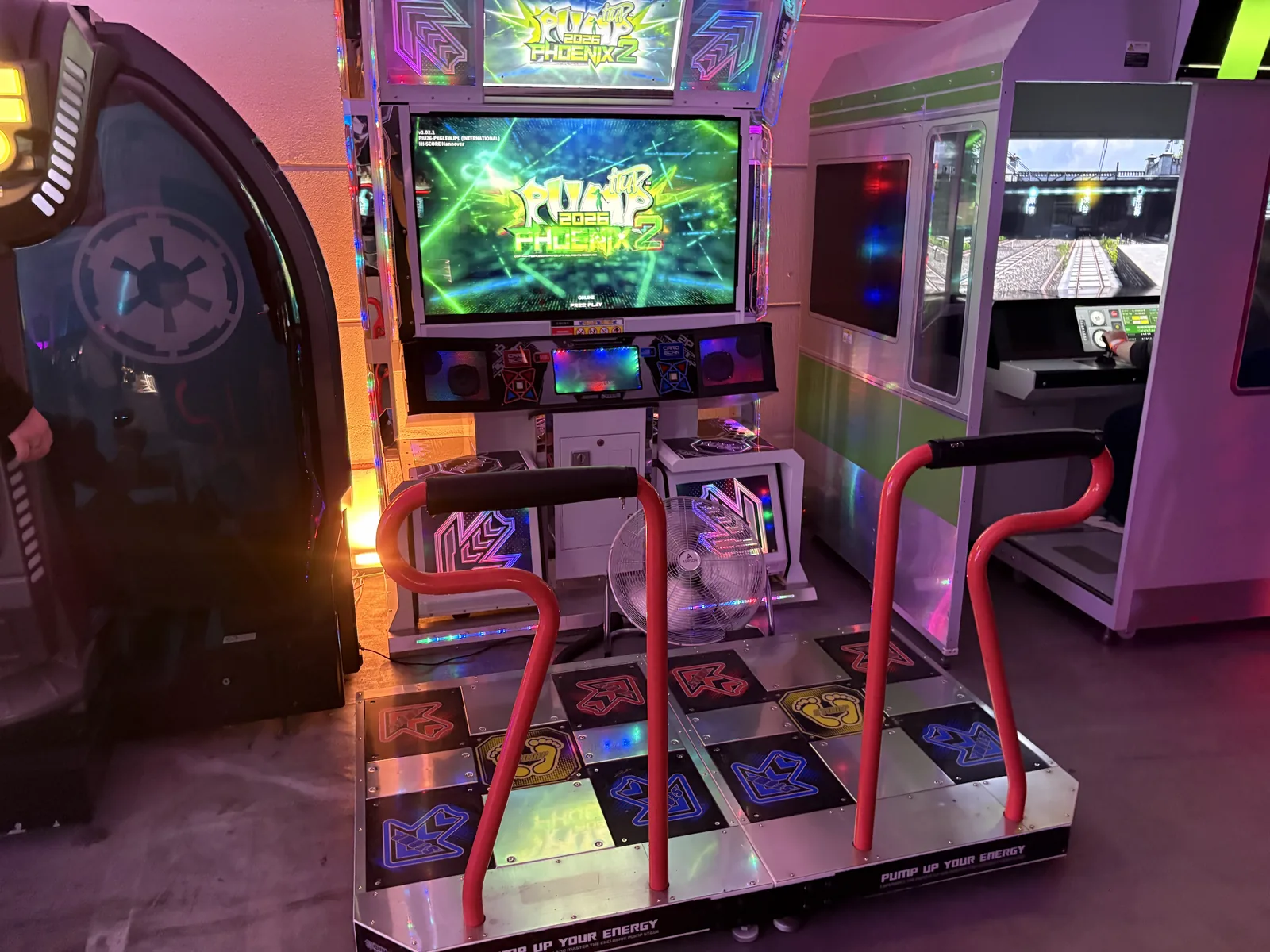 A Pump It Up Phoenix dance arcade machine with a glowing step pad and red safety bars.