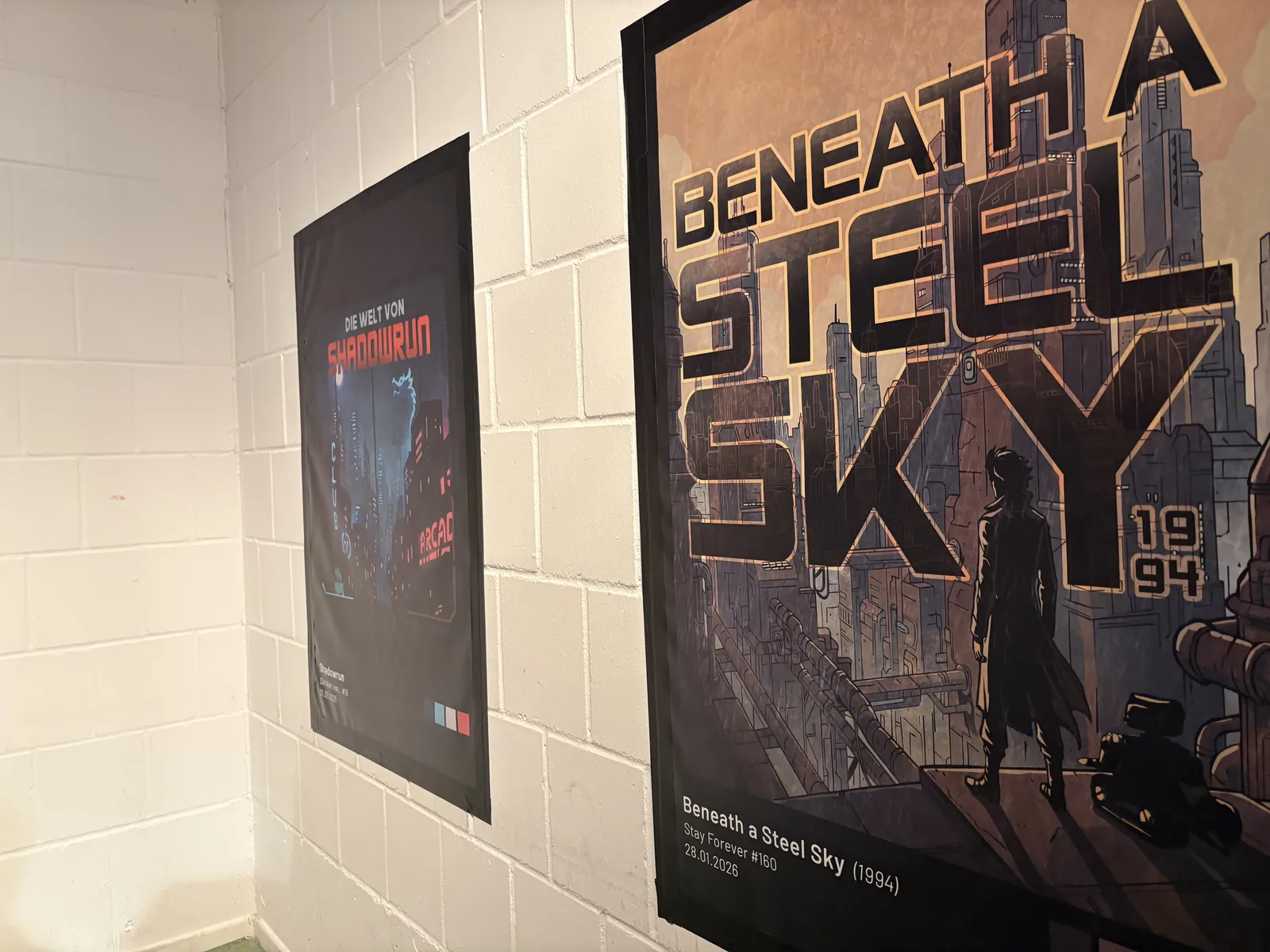 Two large posters on a white brick wall, one for Shadowrun and one for Beneath a Steel Sky, 1994.
