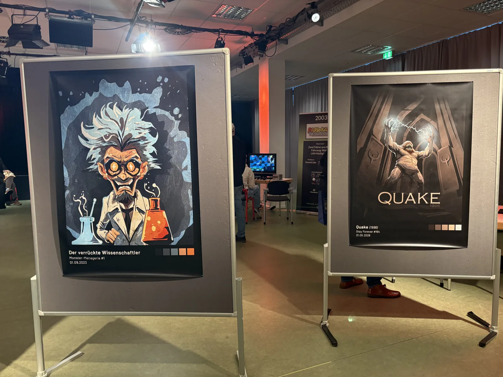Two posters on stands: a cartoon mad scientist with wild white hair, and a Quake poster.