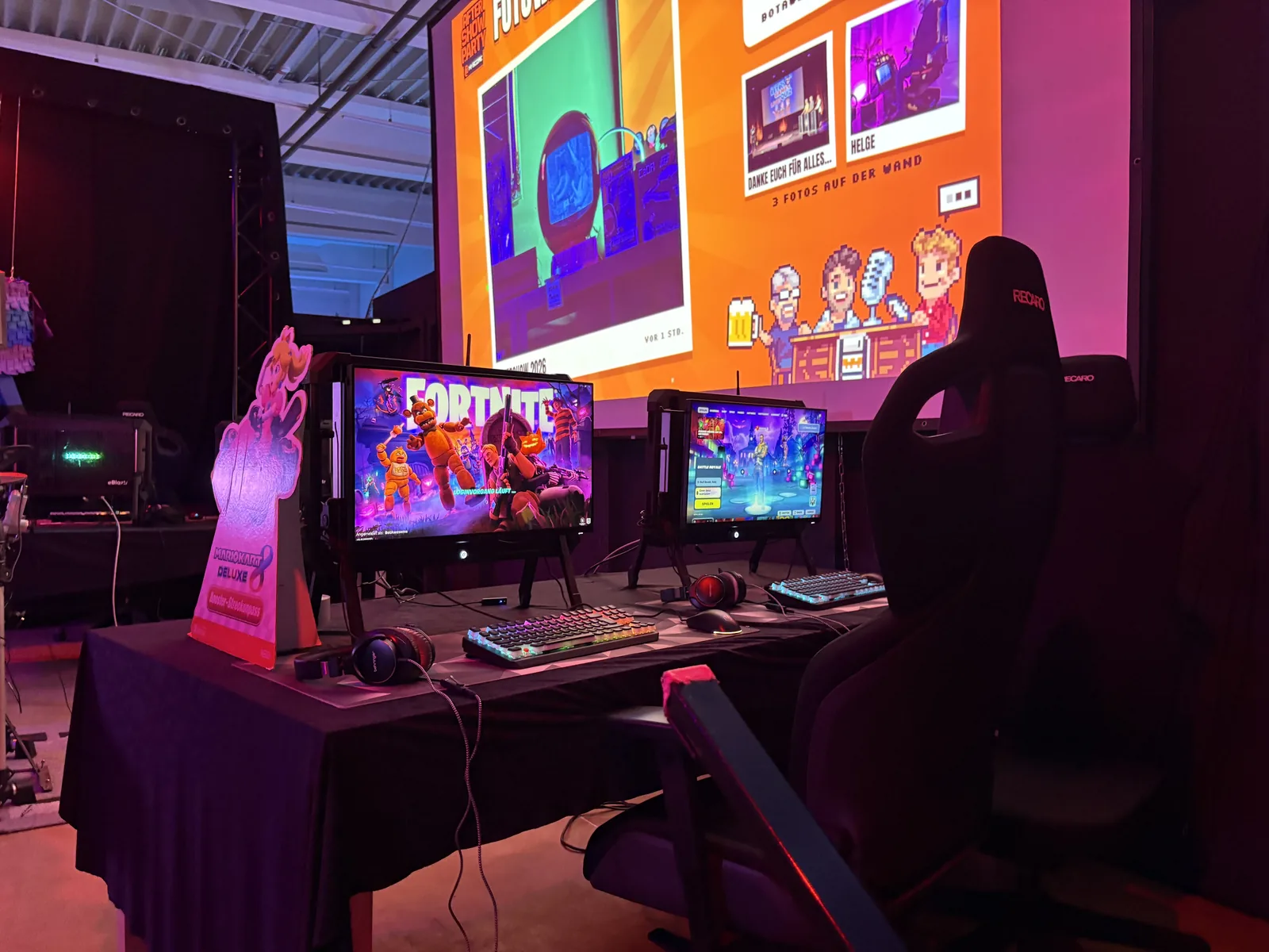 A modern gaming PC setup with Fortnite on screen and a gaming chair, on a stage in front of a big projection.