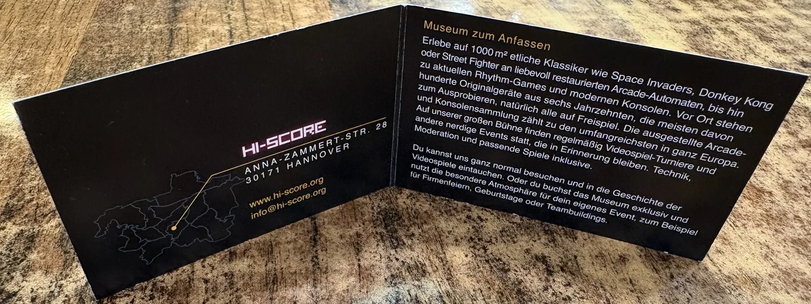 A folded black HI-SCORE card describing the museum, standing on a marble-patterned table.