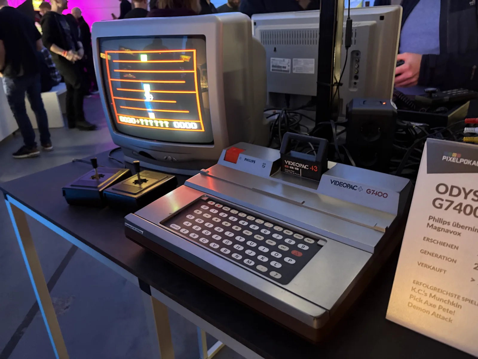 A Philips Videopac G7400 console with a built-in keyboard, connected to a CRT monitor, with an info card beside it.