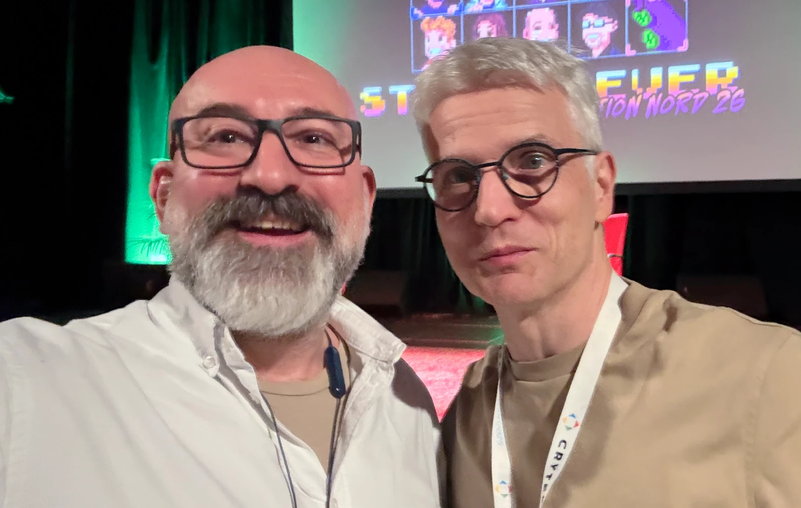 Marin and Gunnar Lott smiling for a selfie in front of the stage screen showing the Stay Forever logo and pixel art portraits.