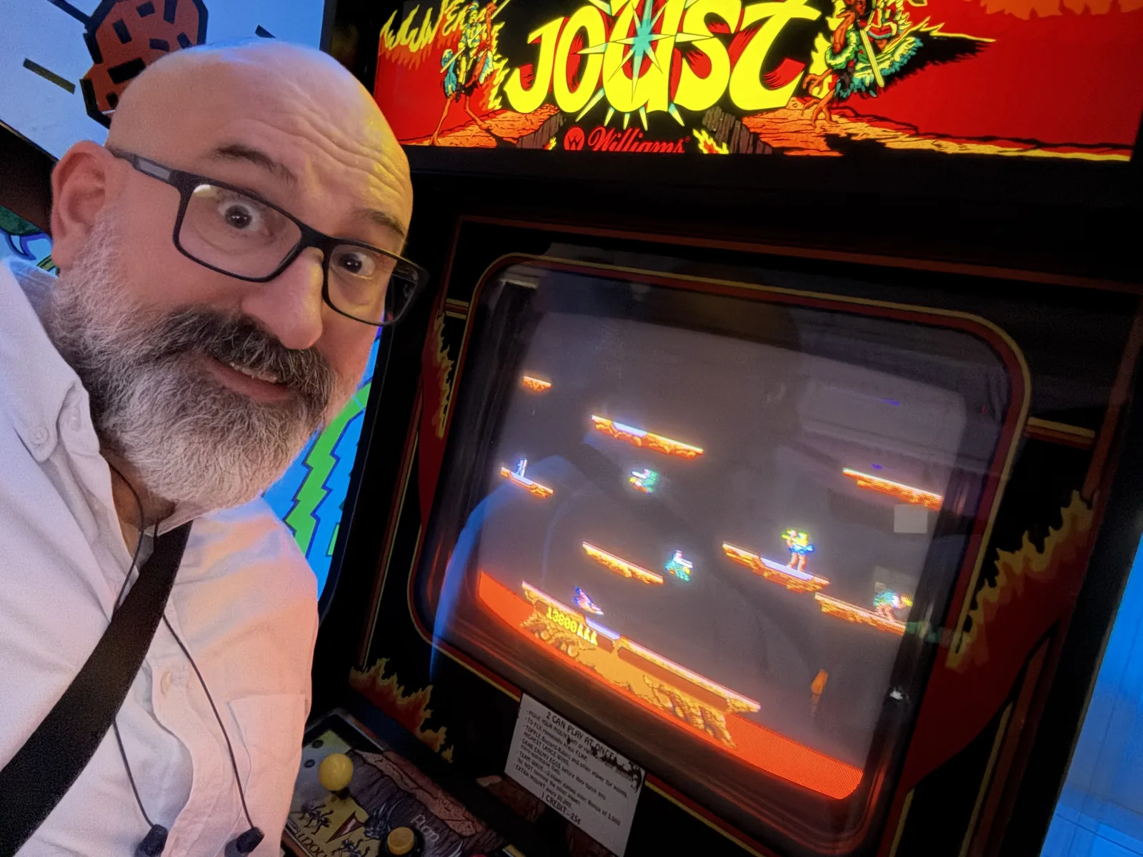 Marin taking a selfie with a wide-eyed expression next to a Joust arcade cabinet.