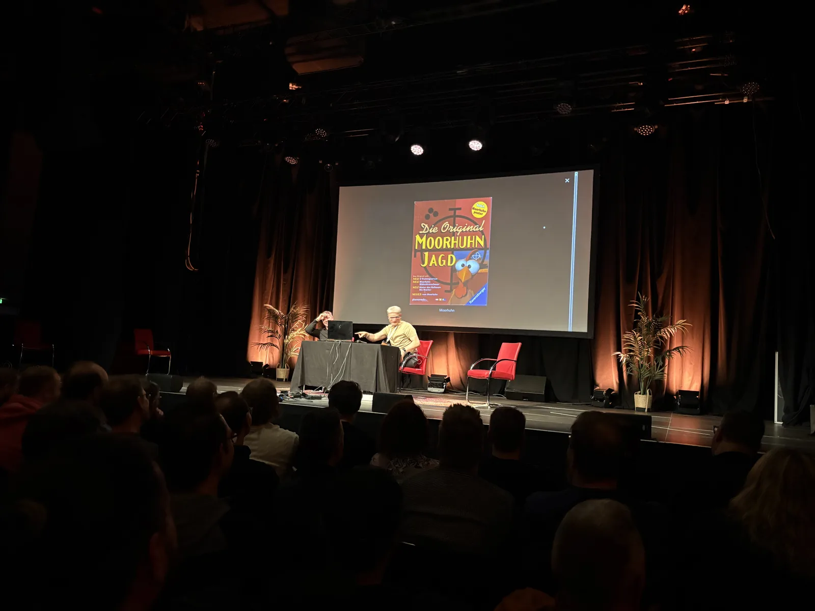 Chris and Gunnar on stage at a desk while the box art of Die Original Moorhuhn Jagd is projected behind them.