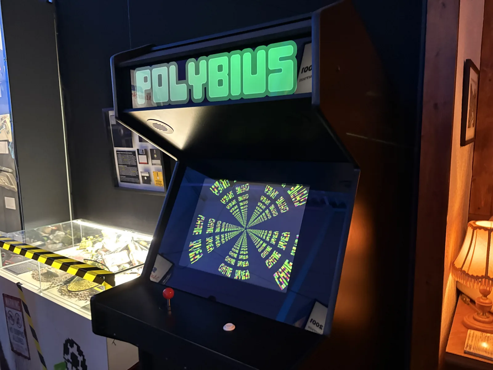 A black Polybius arcade cabinet with a green glowing marquee and a hypnotic spiral on screen.