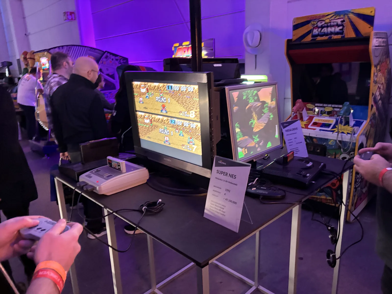 A Super Nintendo and a Sega Mega Drive on a table, each connected to a monitor, with visitors playing.