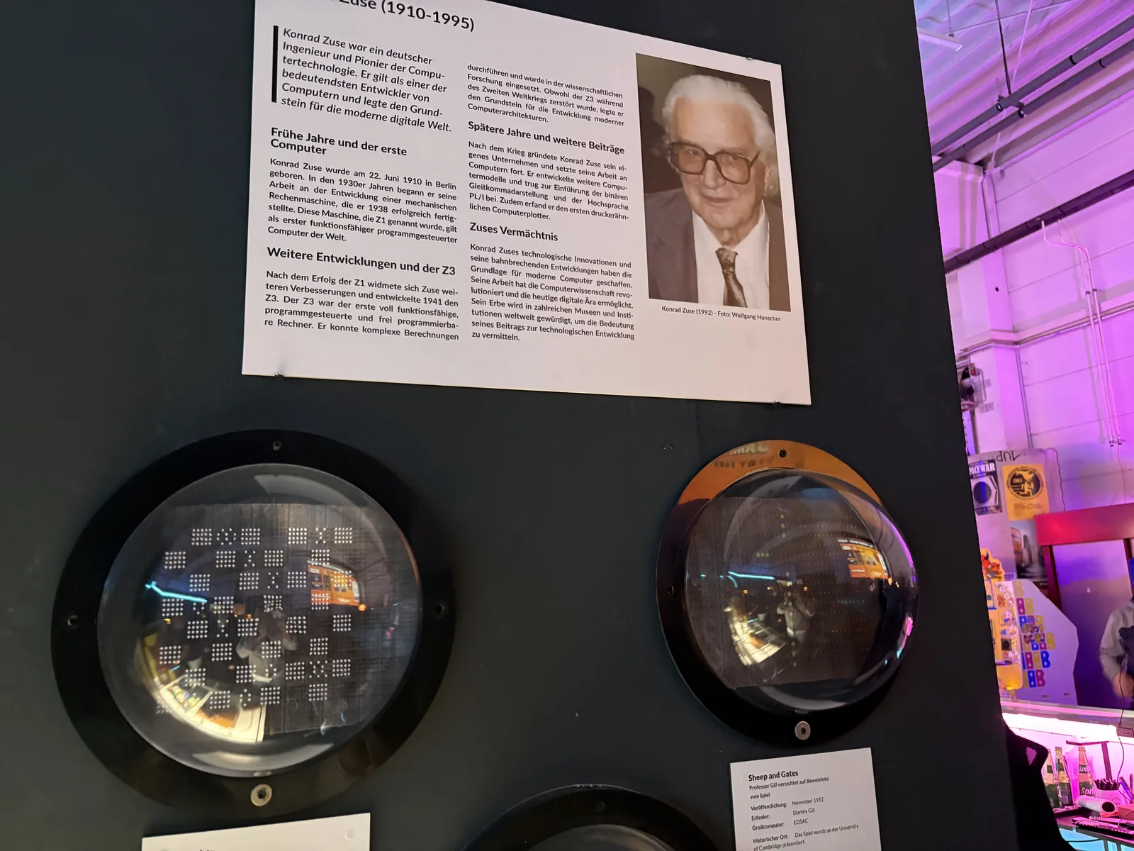 A wall panel with a biography and photo of Konrad Zuse above round glass portholes showing old computer components.