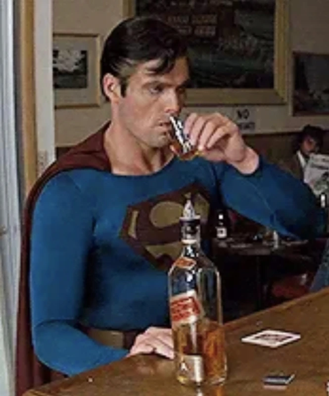 Christopher Reeve as a dishevelled Superman drinking whisky at a bar in Superman III, with a half-empty bottle in front of him.
