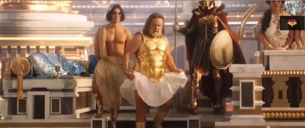 Russell Crowe as Zeus in a gold breastplate, lifting the hem of his short white pleated skirt in Thor: Love and Thunder.